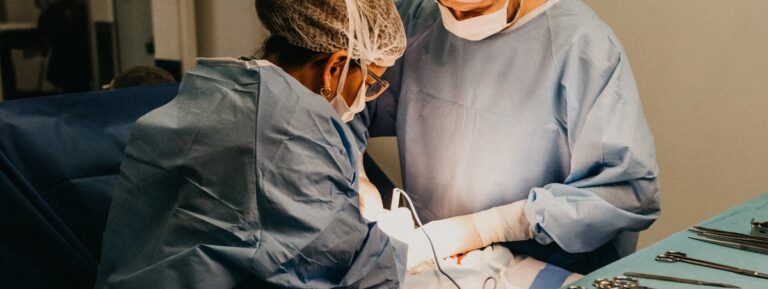 Two surgeons in an operating room conducting surgery under bright lights.